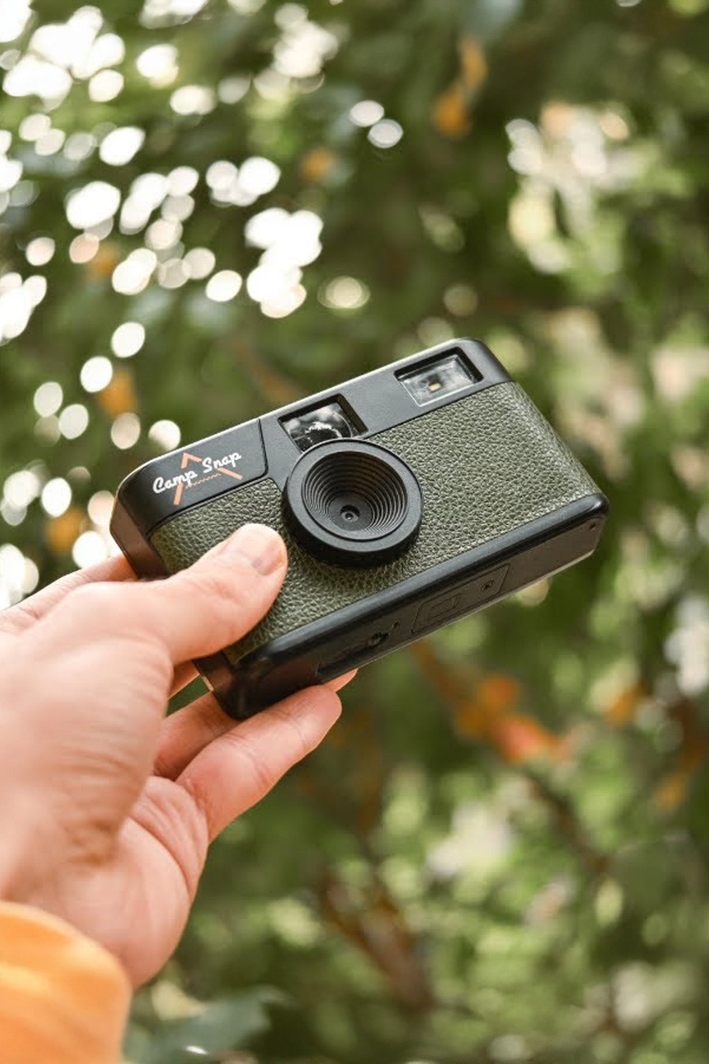 Hand holding a green campsnap camera with a blurred natural background